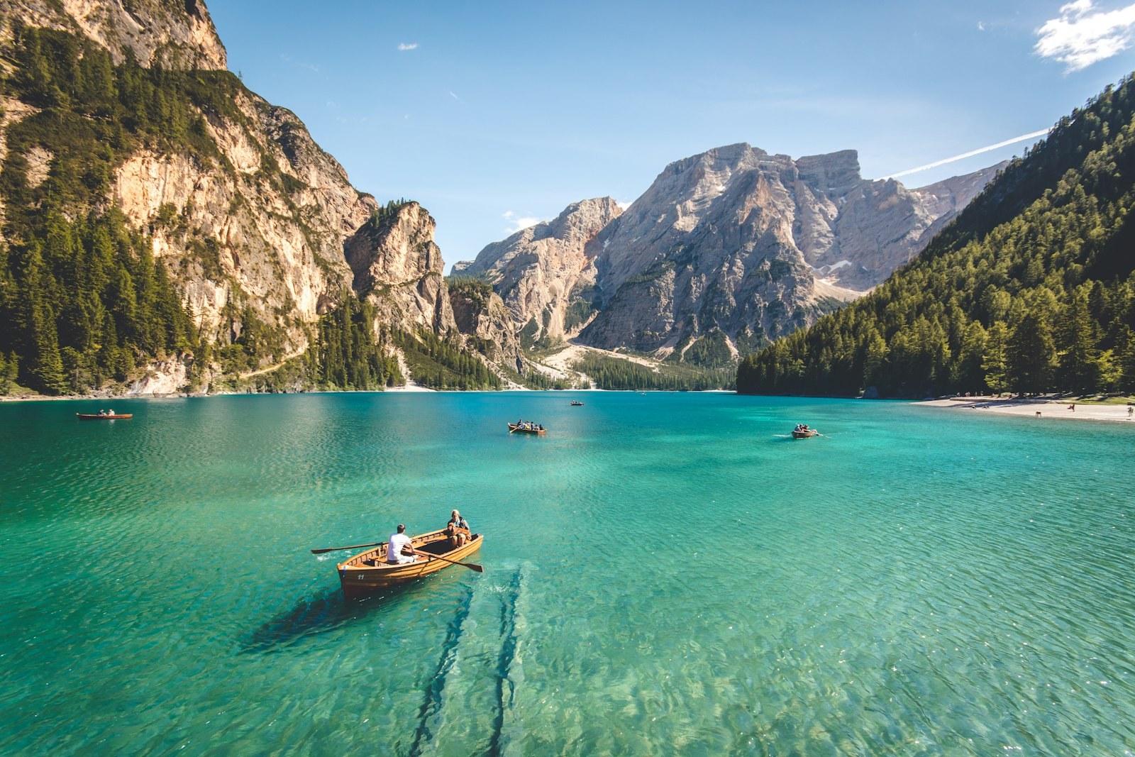 Rowing boats on a turquoise alpine lake beneath forested peaks
